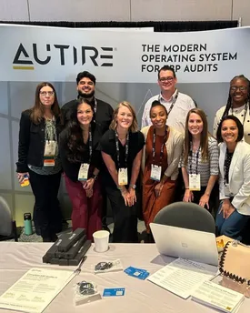 The Autire team standing together at a trade show booth, beneath a banner reading “The modern operating system for ERP audits”.