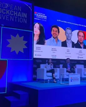 A panel discussion on stage at the European Blockchain Convention in Barcelona, Kadena among the speakers on the screen behind.
