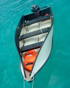 A folding Portabote dinghy seen from above on clear turquoise water, outboard motor fitted and life jackets aboard.
