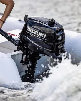 A Suzuki four-stroke outboard motor on the transom of an inflatable boat, throwing up spray under way.