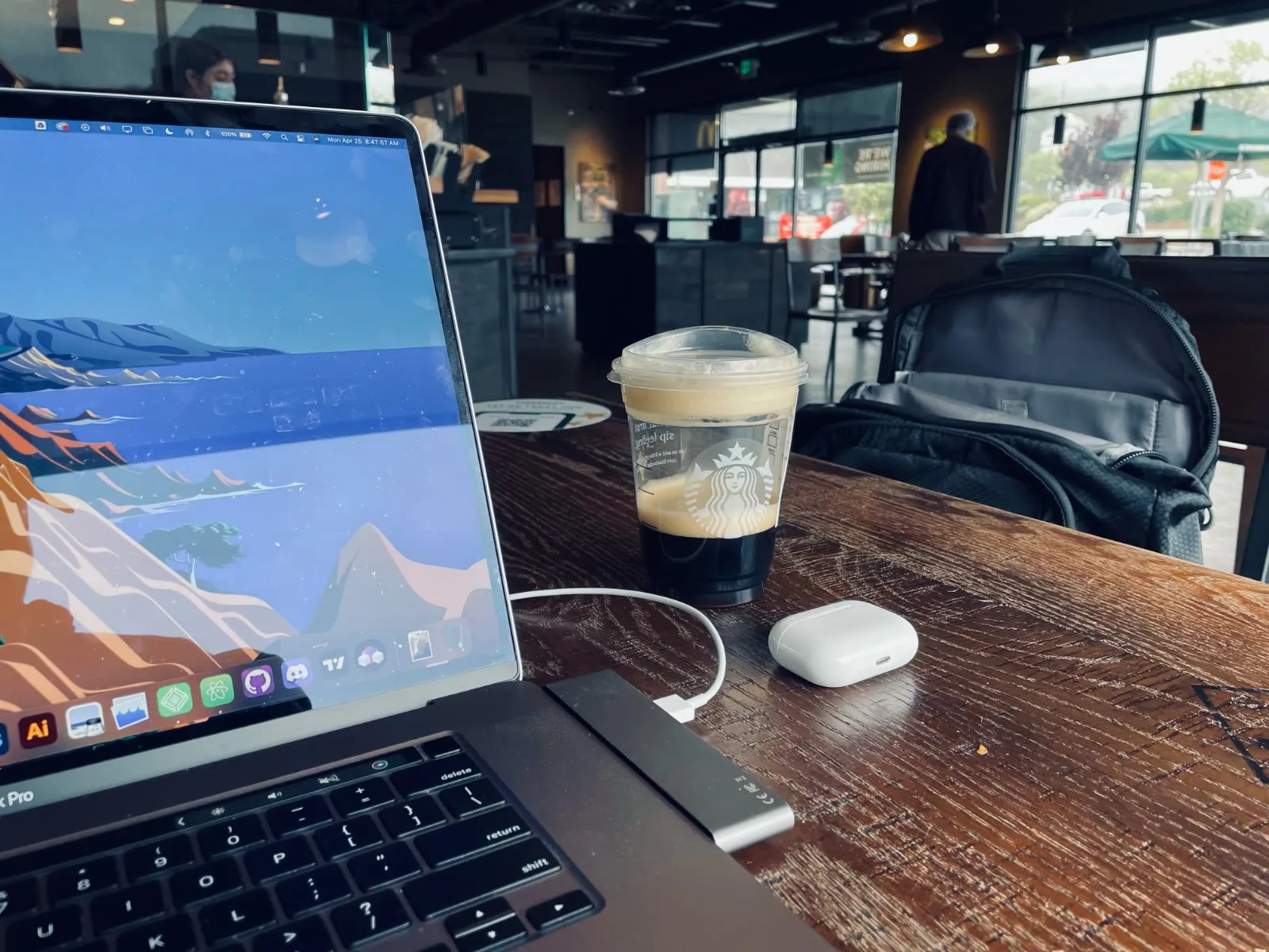 My laptop set up for a morning of remote work in a Prunedale, California café, an iced coffee and AirPods beside it.